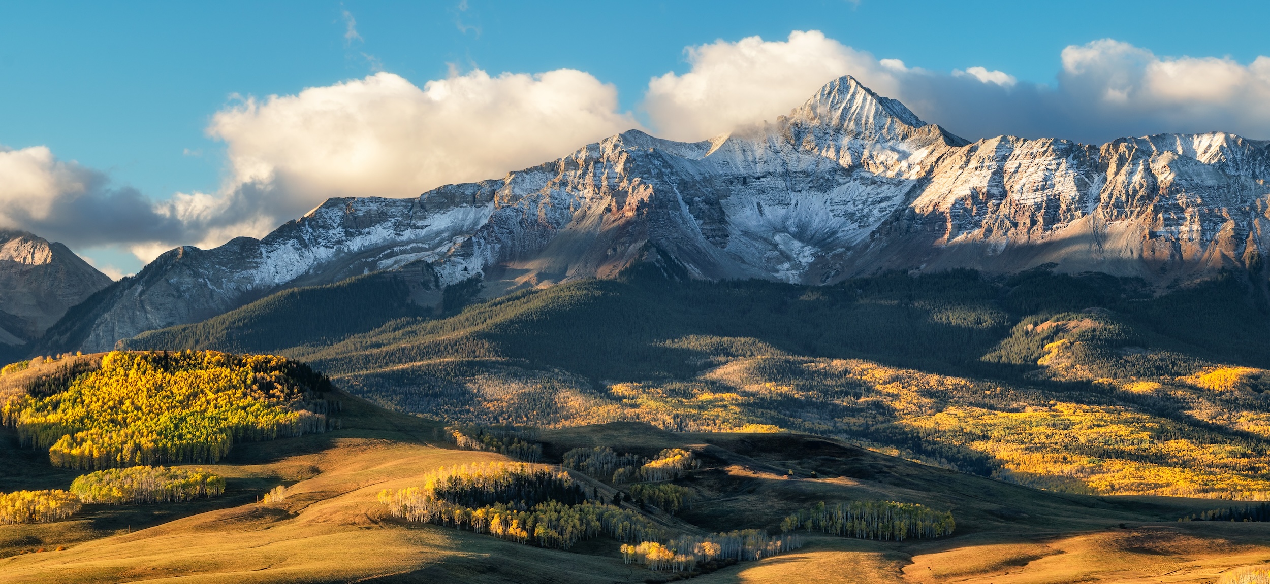 land in rural southwest Colorado with snow-covered peaks in the background, being kissed by puffy white clouds