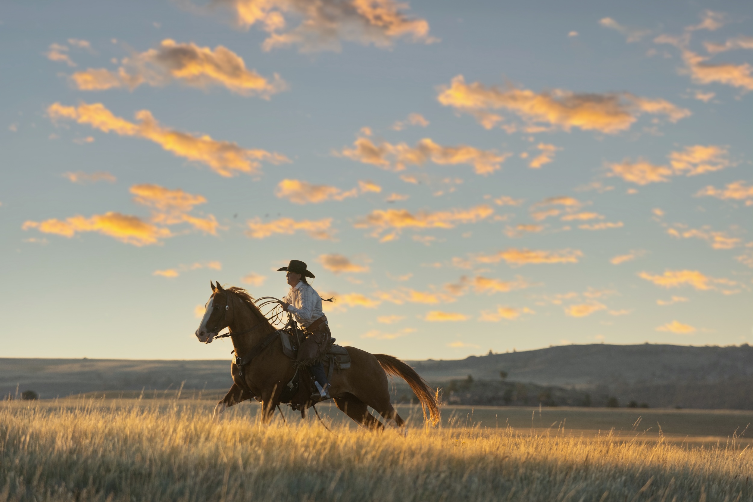 cowgirl riding a horse through her ranch land at sunset