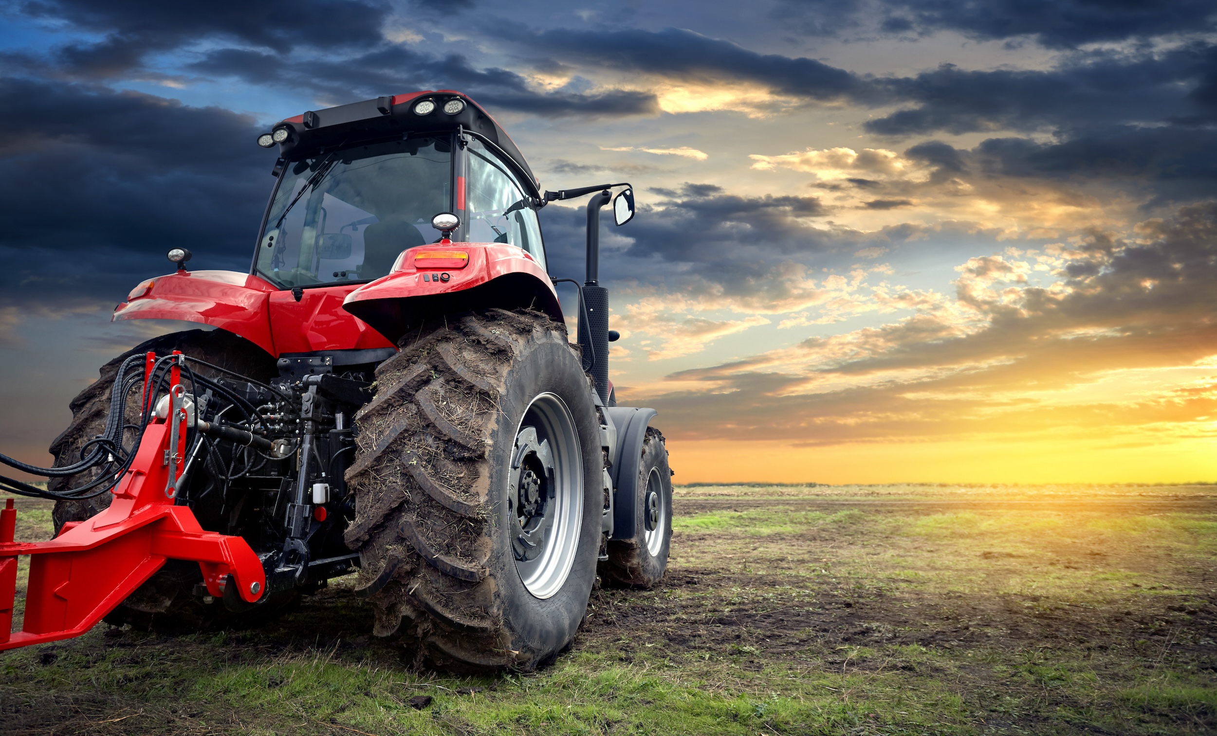 red tractor with thick large size wheels driving through grassy and muddy terrain