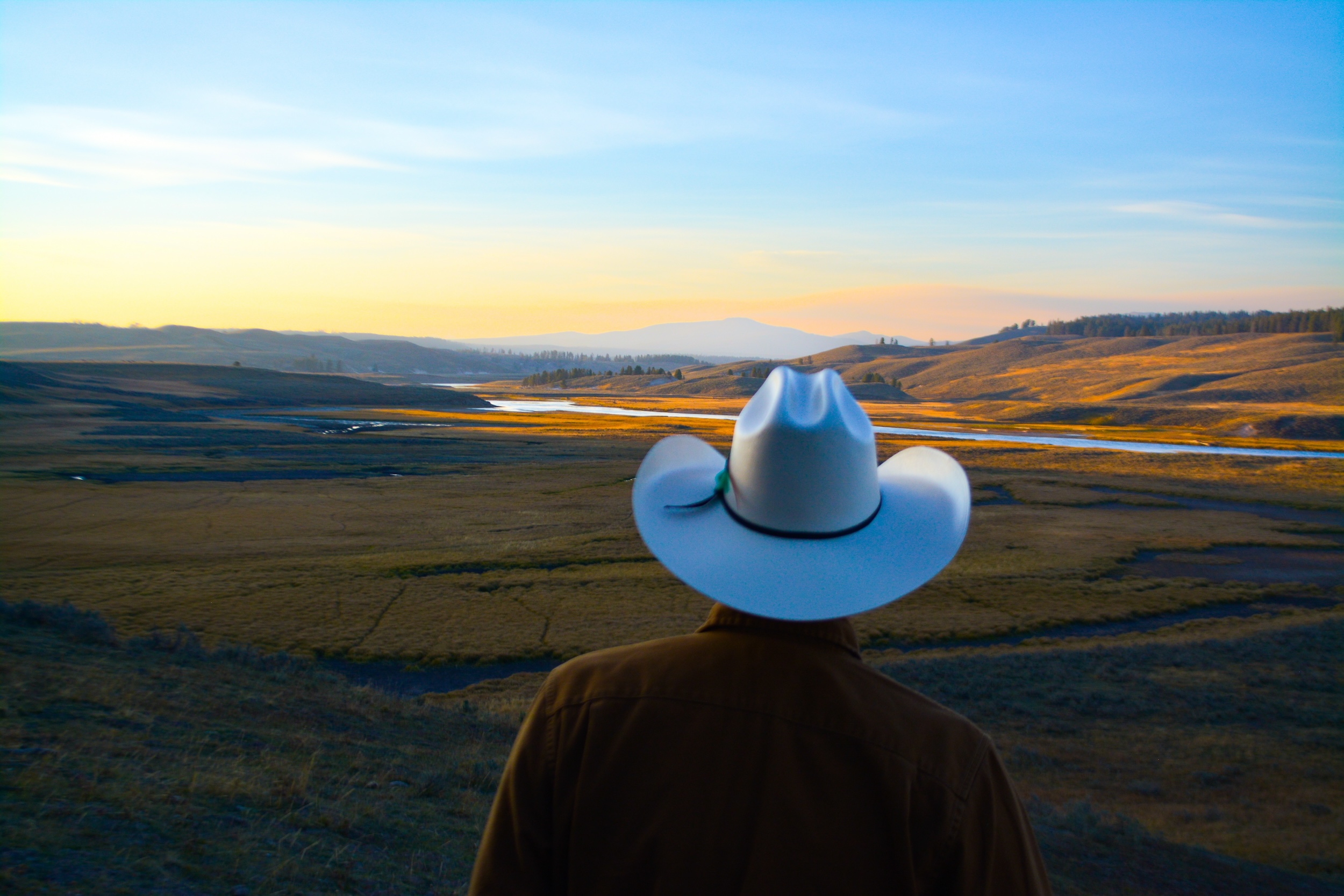 cowboy in a white hat living on a ranch looking out on his land during sunset