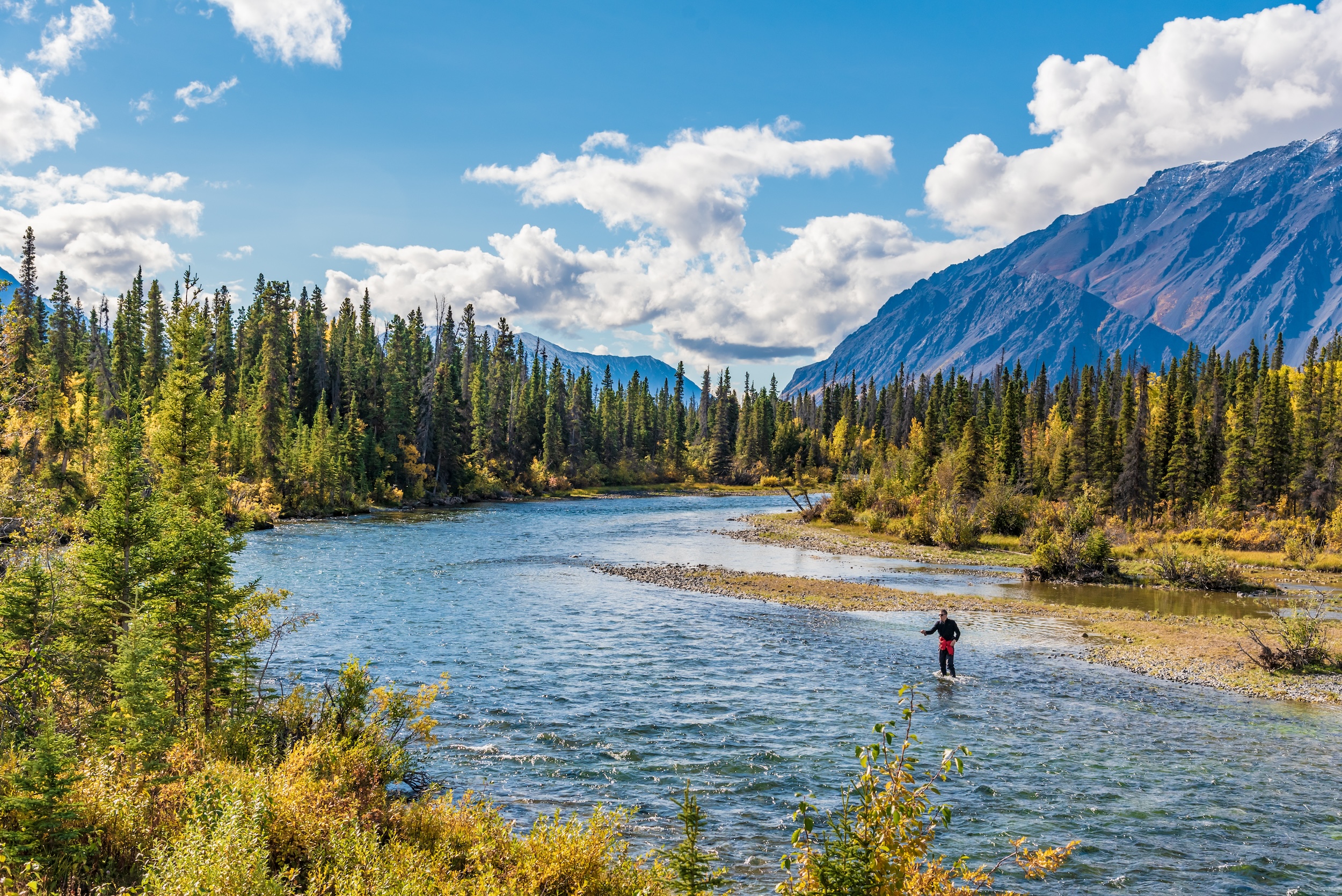 man standing in a river in the mountains showing off his fly fishing techniques and basics