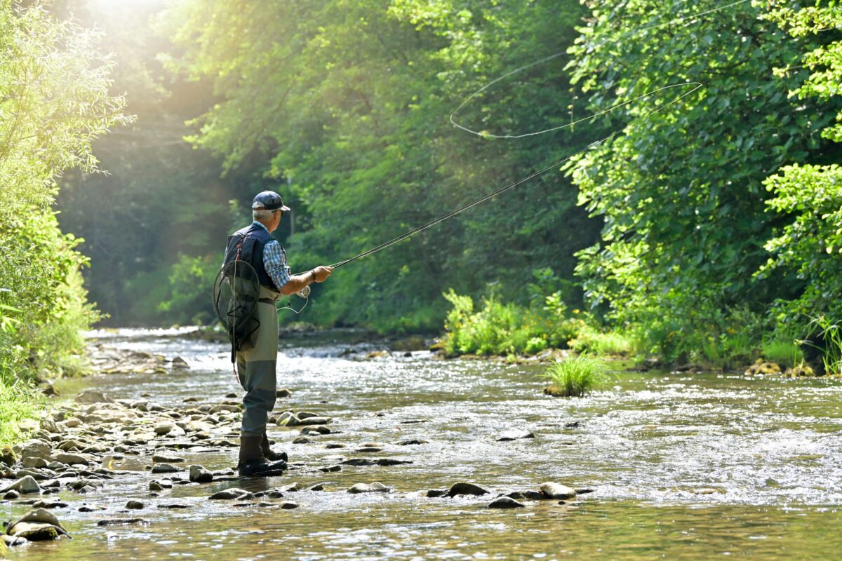 man standing near the shore of a river performing the overhead cast fly fishing technique method