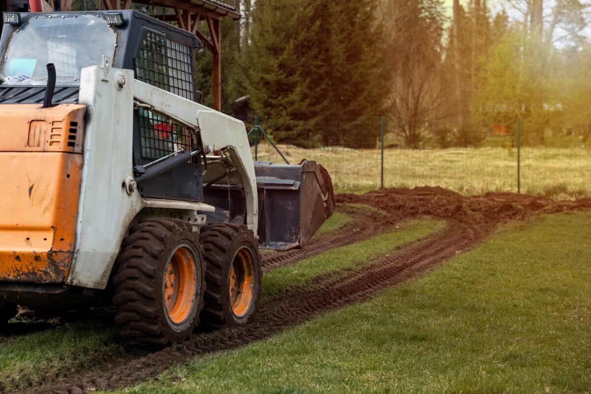 a white skid steer being used to move dirt on a farm property