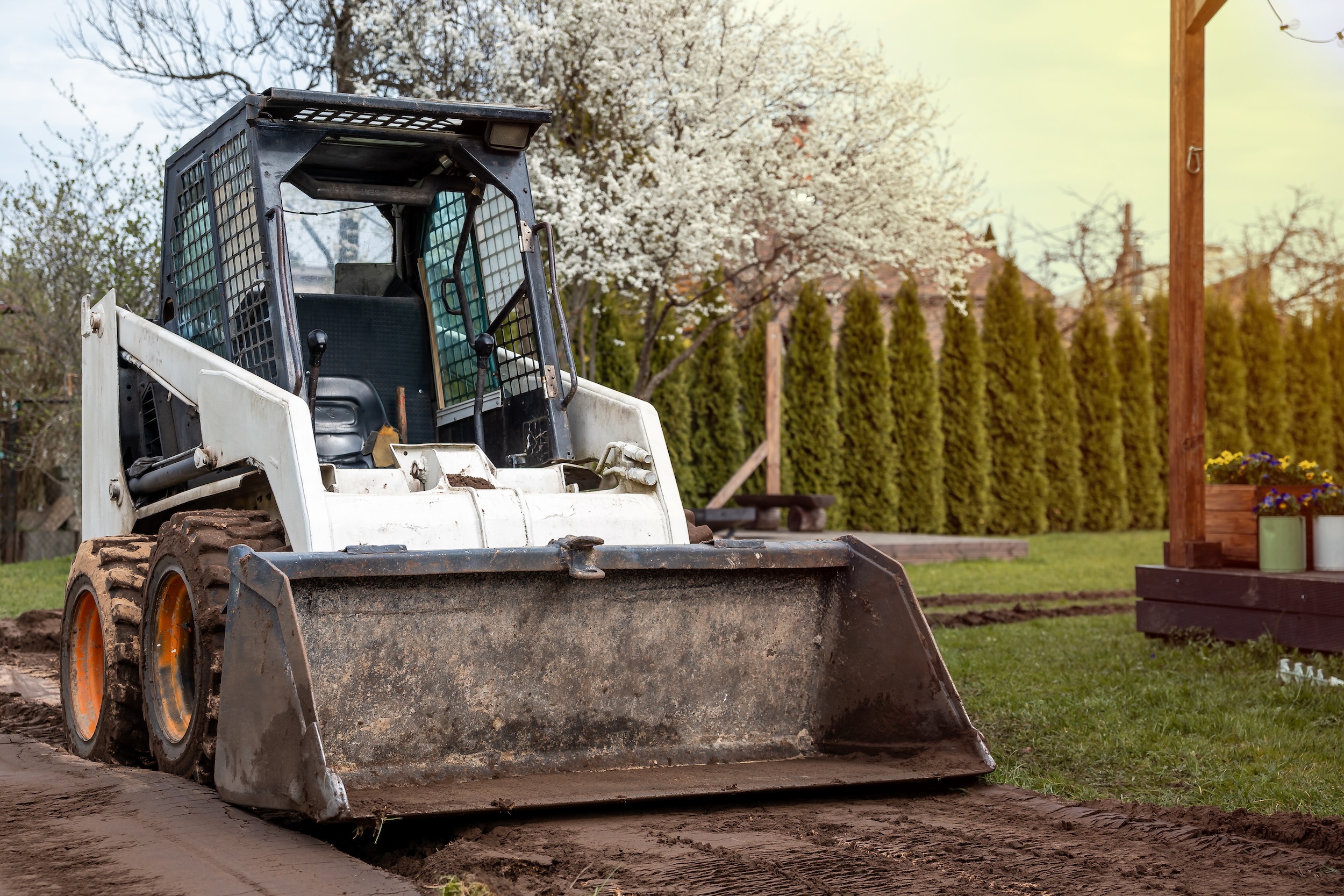 skid steer with wheels being used to clear a path for landscaping in a yard