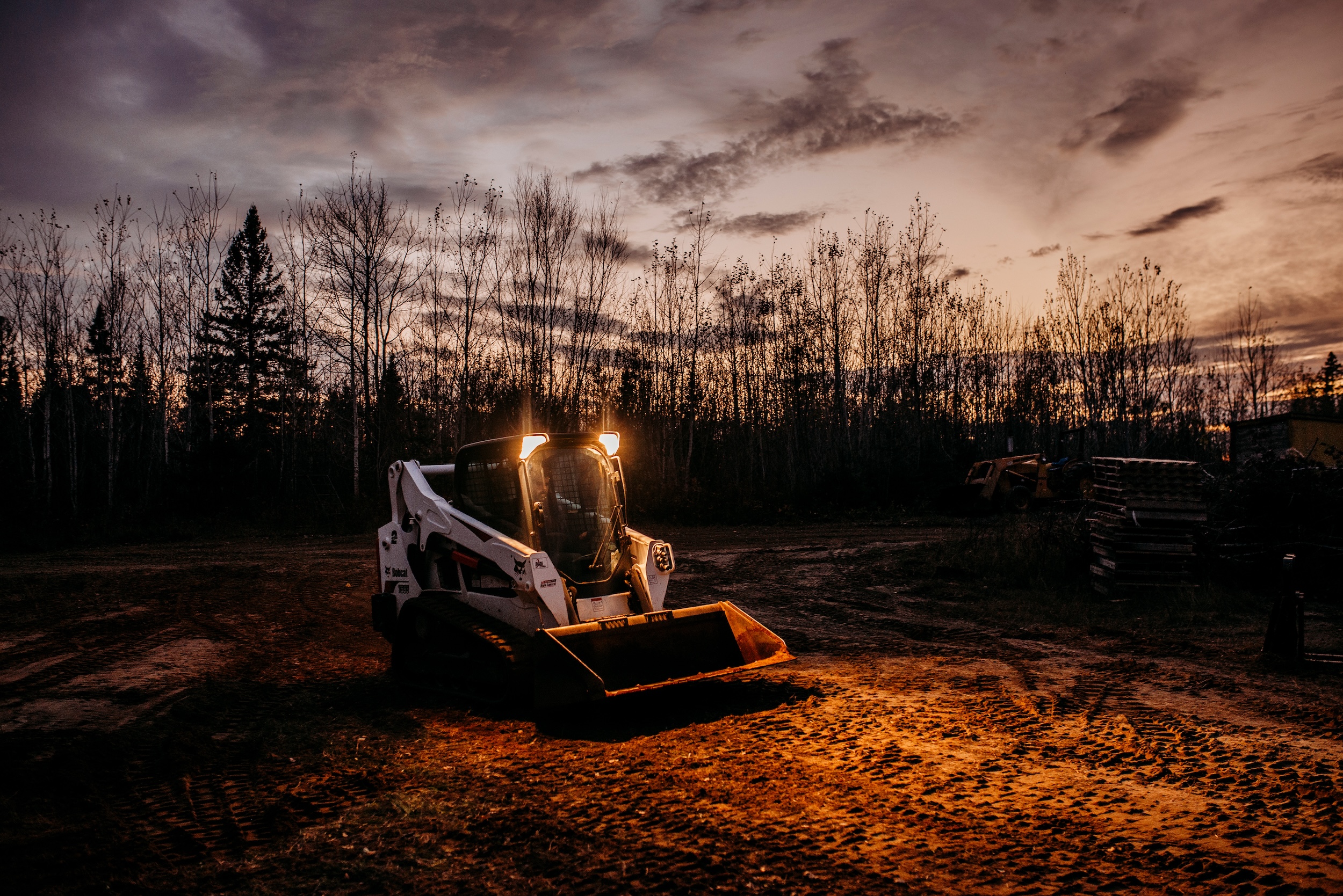 a skid steer showing what it can do by helping to move dirt on a build site in the woods at dawn