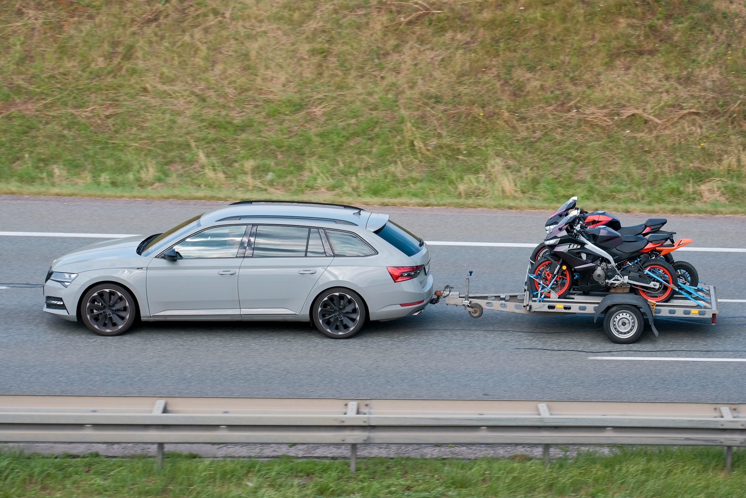 sedan towing motorcycles behind it using a semi trailer