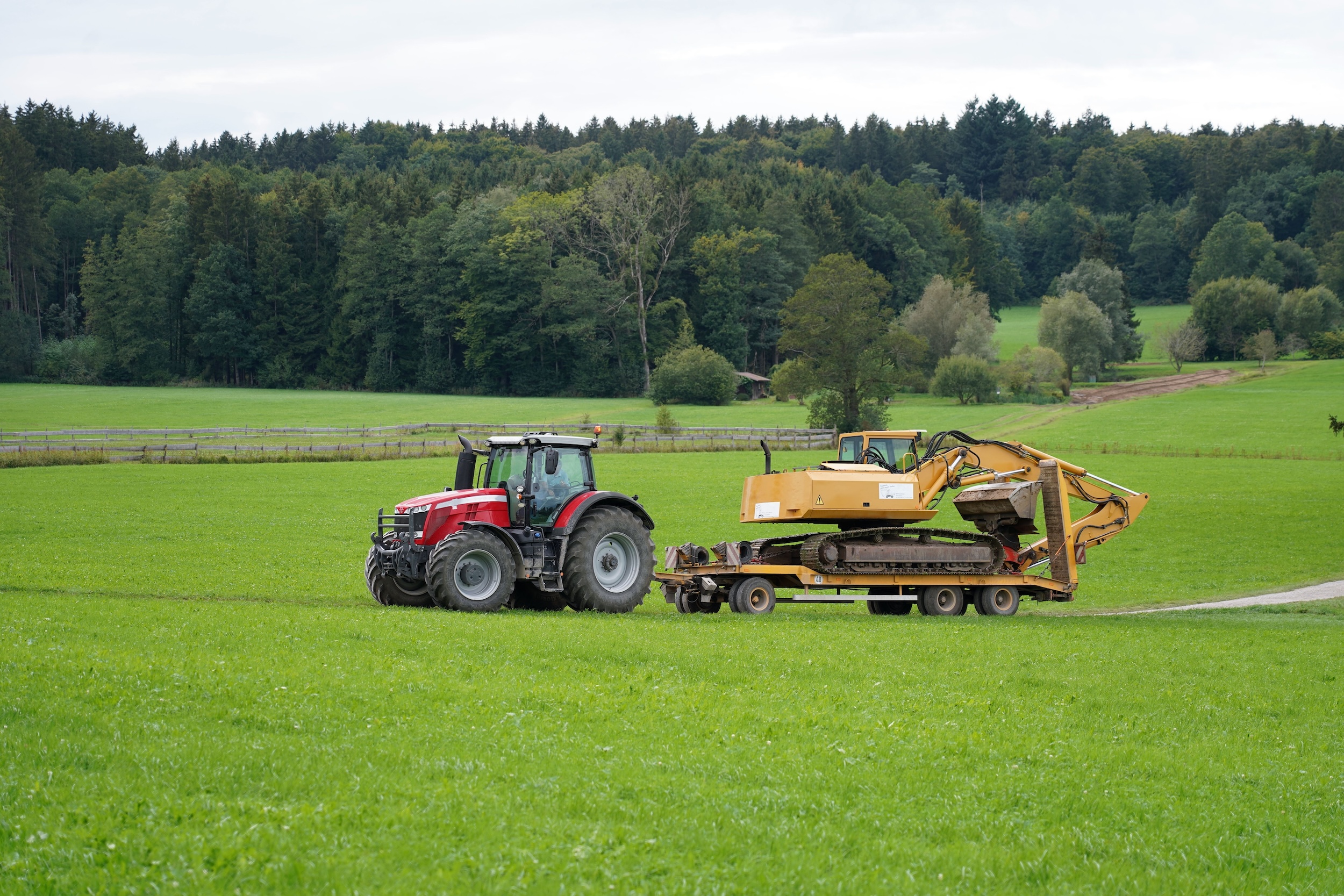 red tractor using a full trailer to tow an excavator across a wide open field on a farm