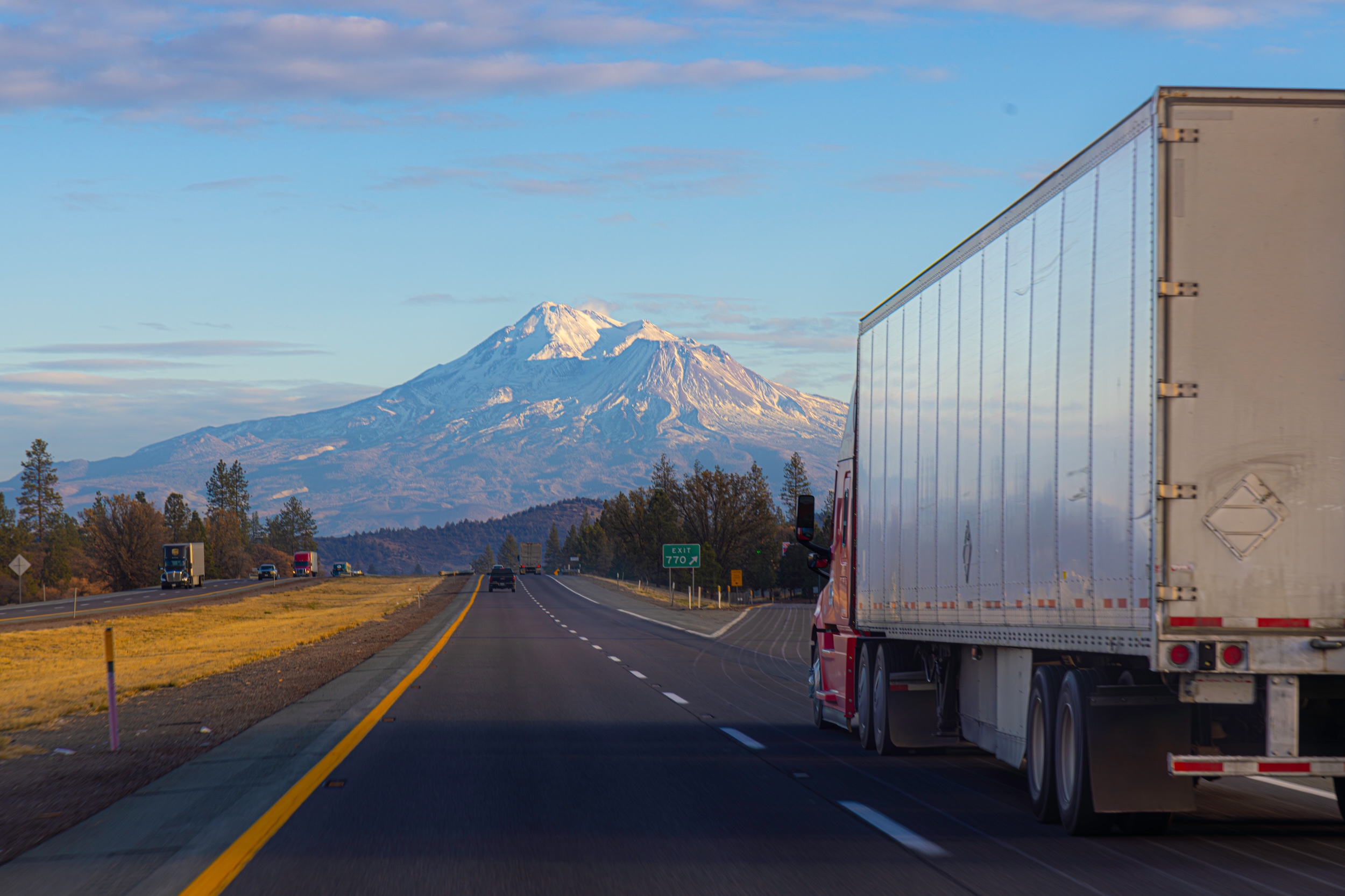 semi truck with a trailer in tow driving on a freeway toward Mount Shasta