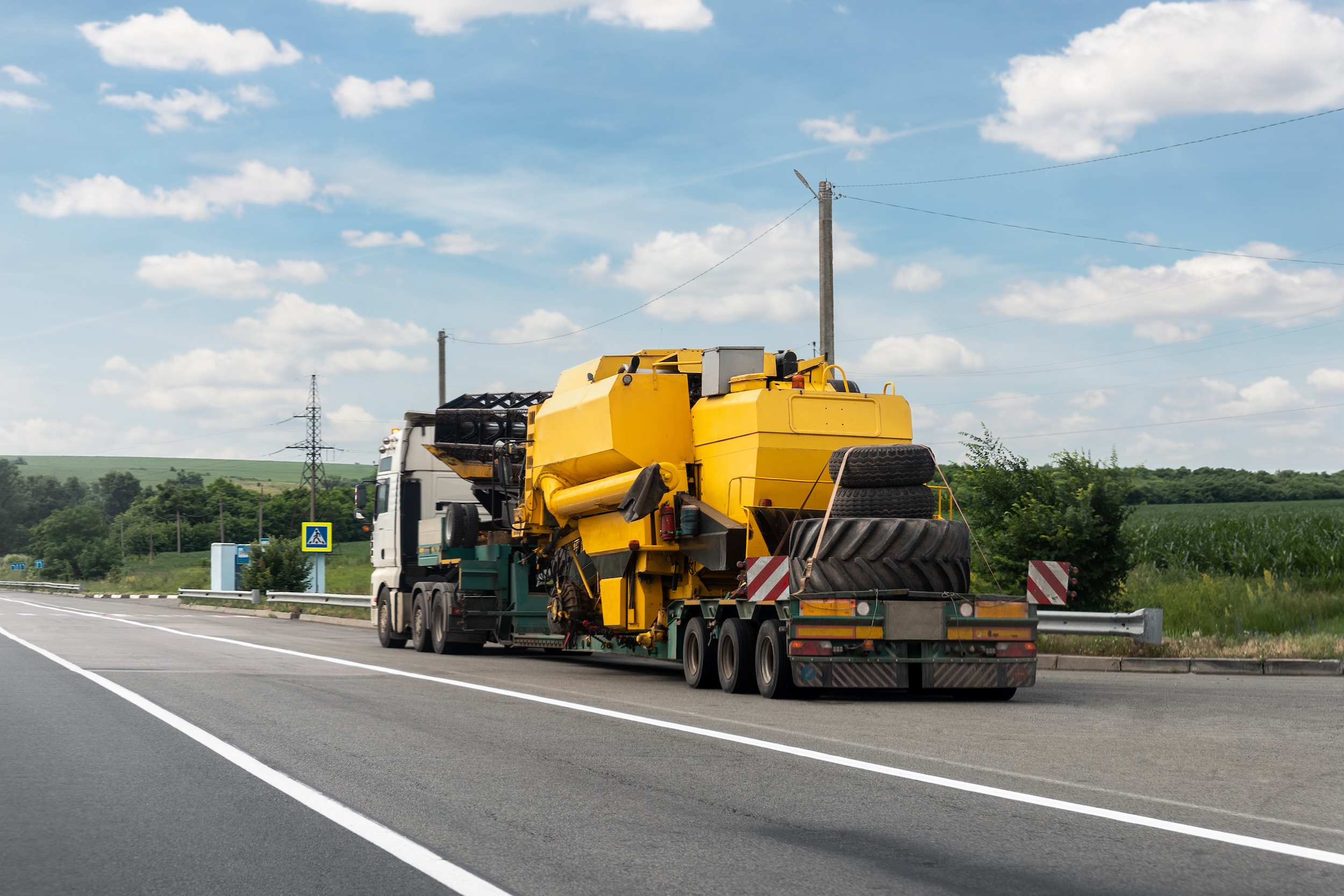 truck with a semi trailer hauling a large piece of yellow equipment on a long haul trip on a highway