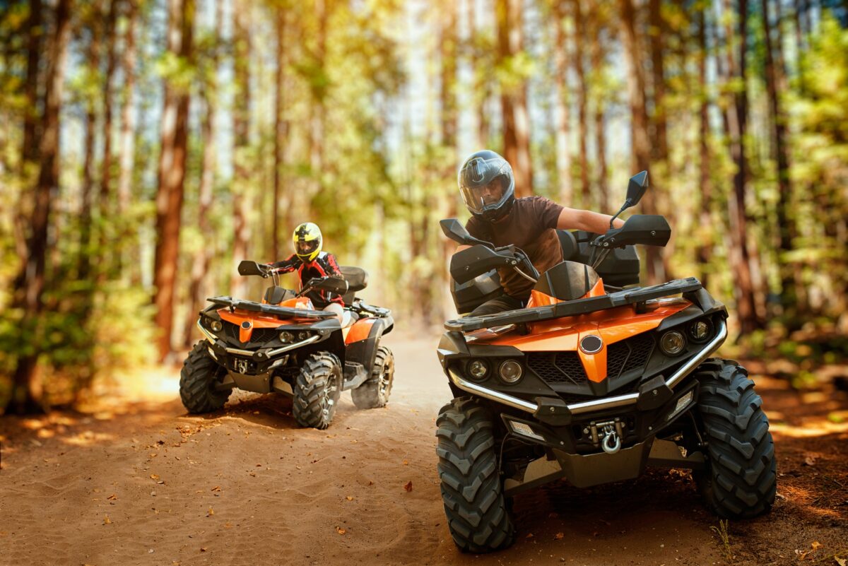 two drivers each riding an atv through a forested trail showing the difference in maneuverability when off-roading vs a utv
