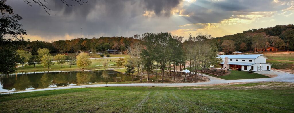view of a ranch property with a large white barn sitting next to a pond with trees along the shoreline