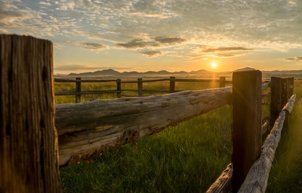 fence around a mountain ranching property with the sun setting behind the peaks