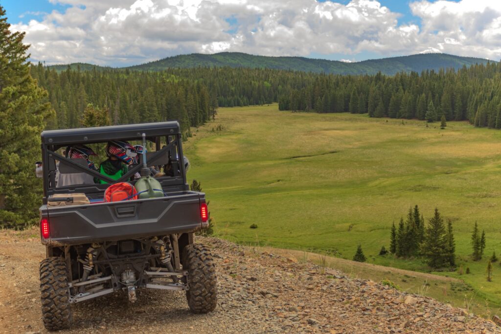 passengers and the driver of a utv wearing helmets as they drive down a dirt mountain road