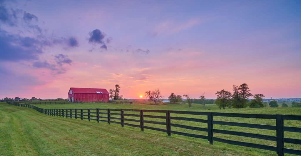 fence on a piece of farmland with a red barn in the background