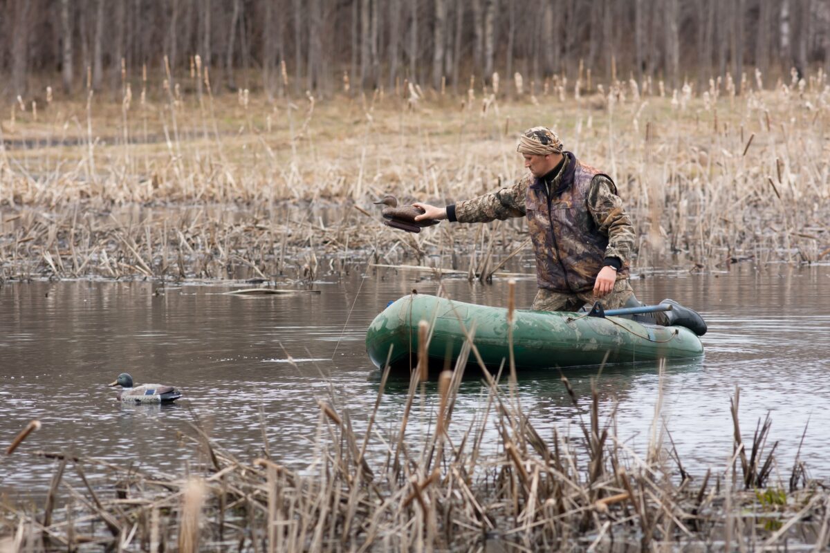 man on a boat in camouflage putting a decoy into the water for duck hunting