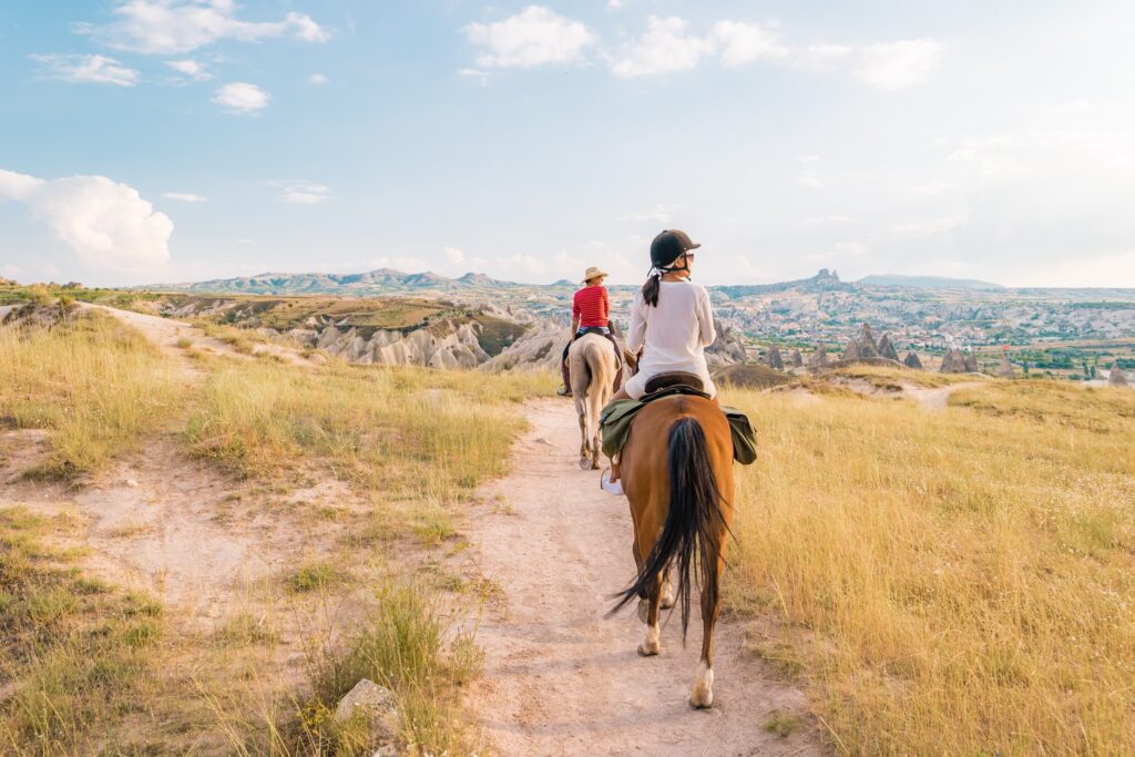 two people riding horses down a trail in the foothills