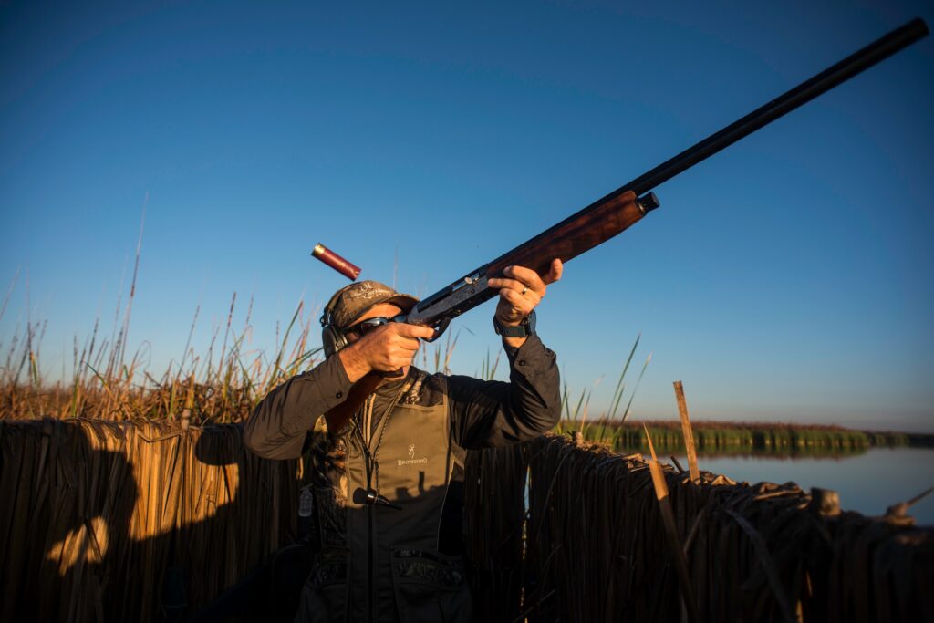 sportsman shooting his shotgun at ducks while hunting on the water in his boat