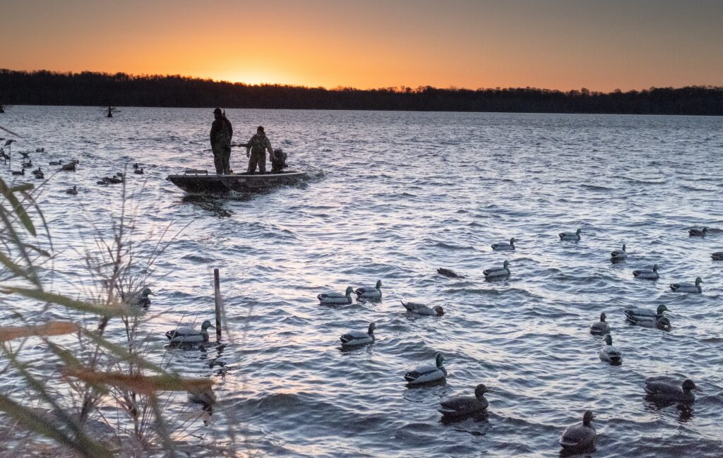 two men in a boat hunting the ducks in the foreground during sunrise
