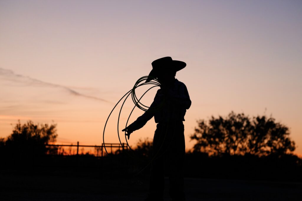 silhouette of a rancher holding a rope while wearing his cowboy hat on his ranch property at dawn