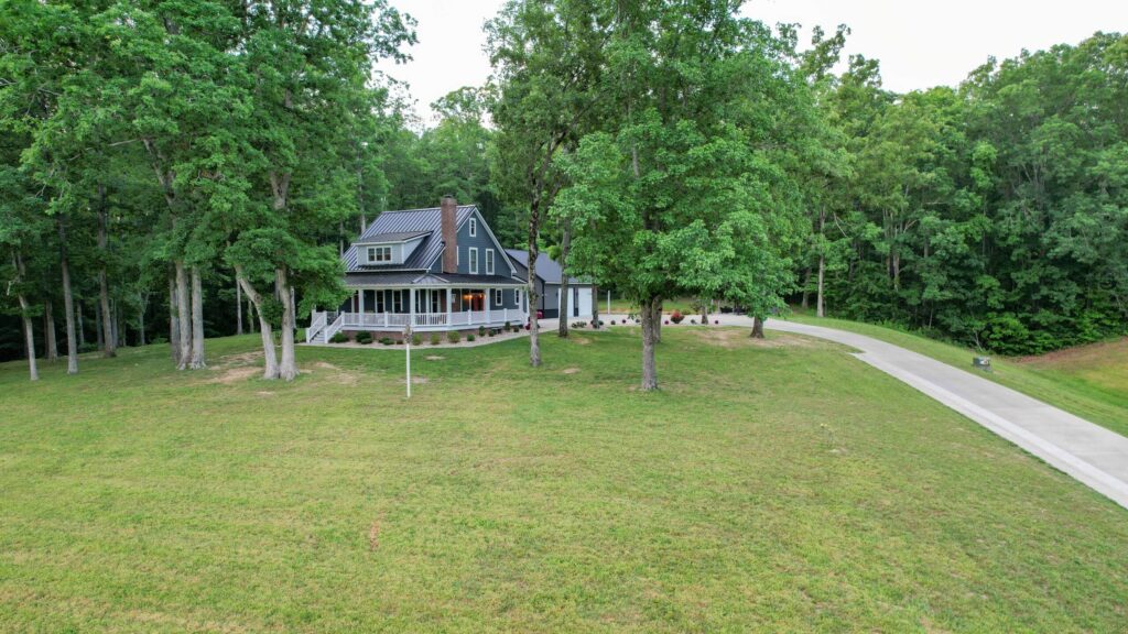 blue southern style house with a large grassy yard and a wraparound porch selling through a good Hayden Outdoors real estate agent