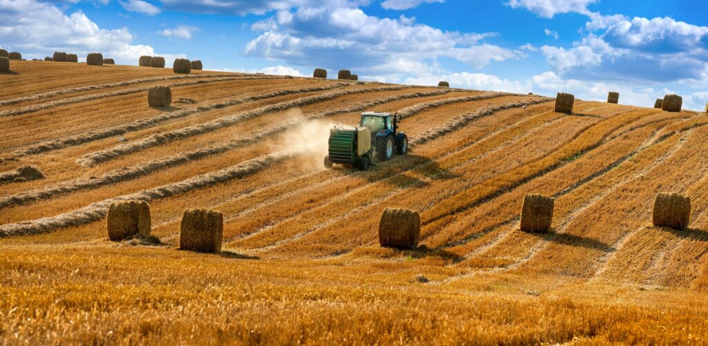 hay baler driving through grass on a farm field during harvest season