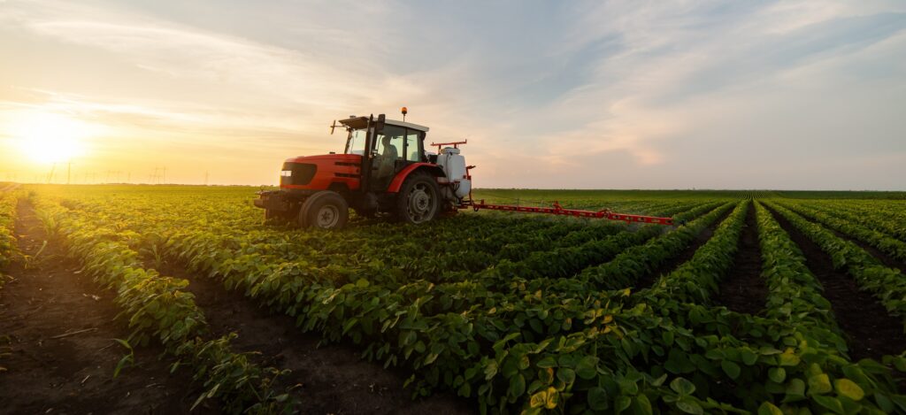 red tractor driving through row crops on a farm showing the difference between farming and ranch operations