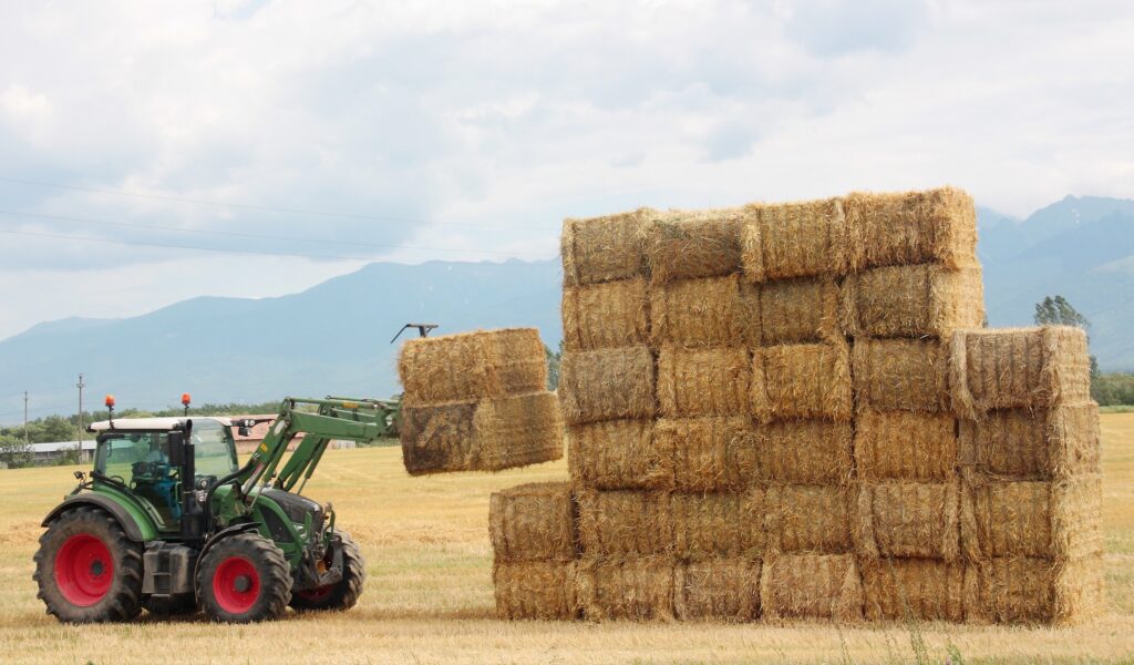 tractor stacking bales of rectangular hay on an open farm field