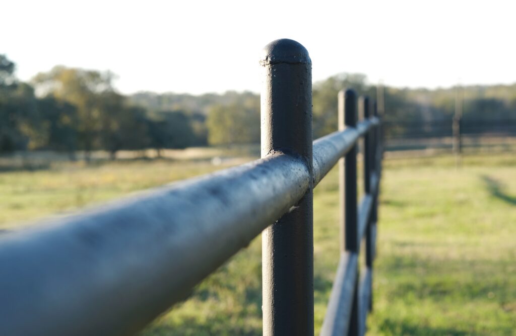 high cost ranch pipe fence installation in an open field on a farm property