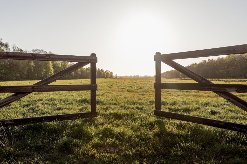 gate on a wood rail fence opening up to a grassy field on a farm