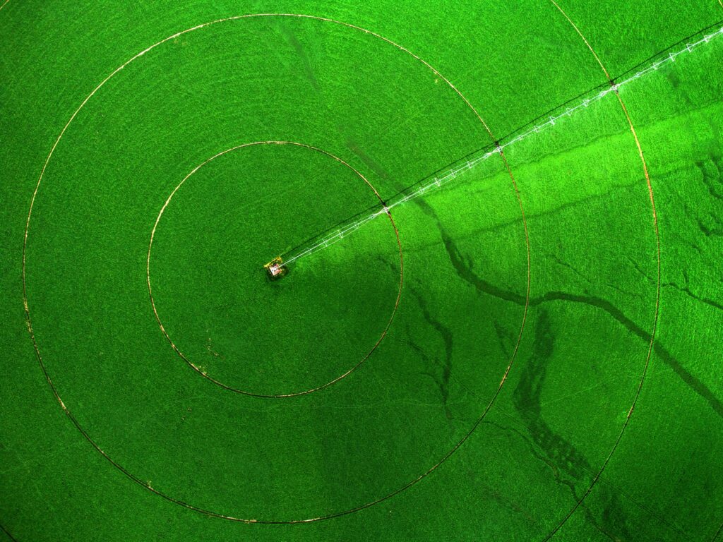 aerial view of a pivot sprinkler crop irrigation system rotating around a large green agricultural field