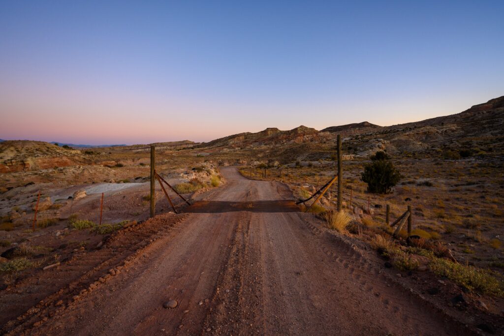 dirt road with a cattle guard traversing it on a ranch that has a wire fencing around the rest of the property