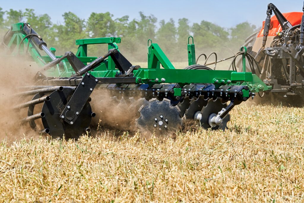green disc harrow going across a wheat field