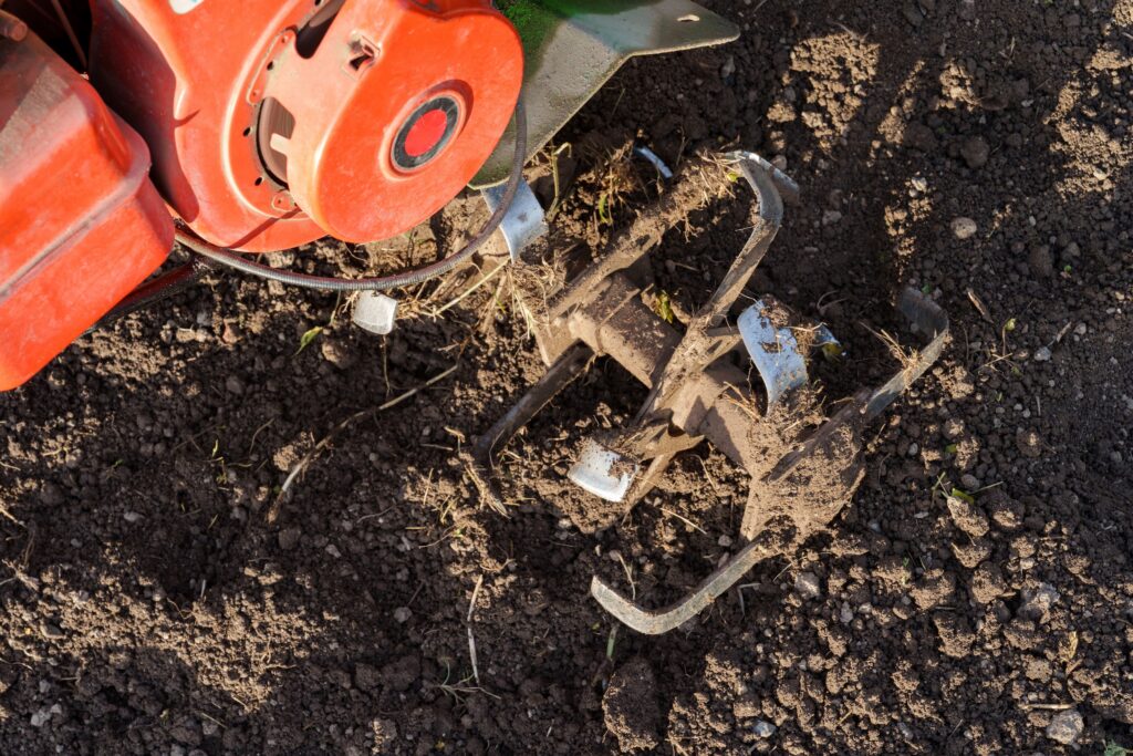 blades of a rototiller tilling soil on a farm